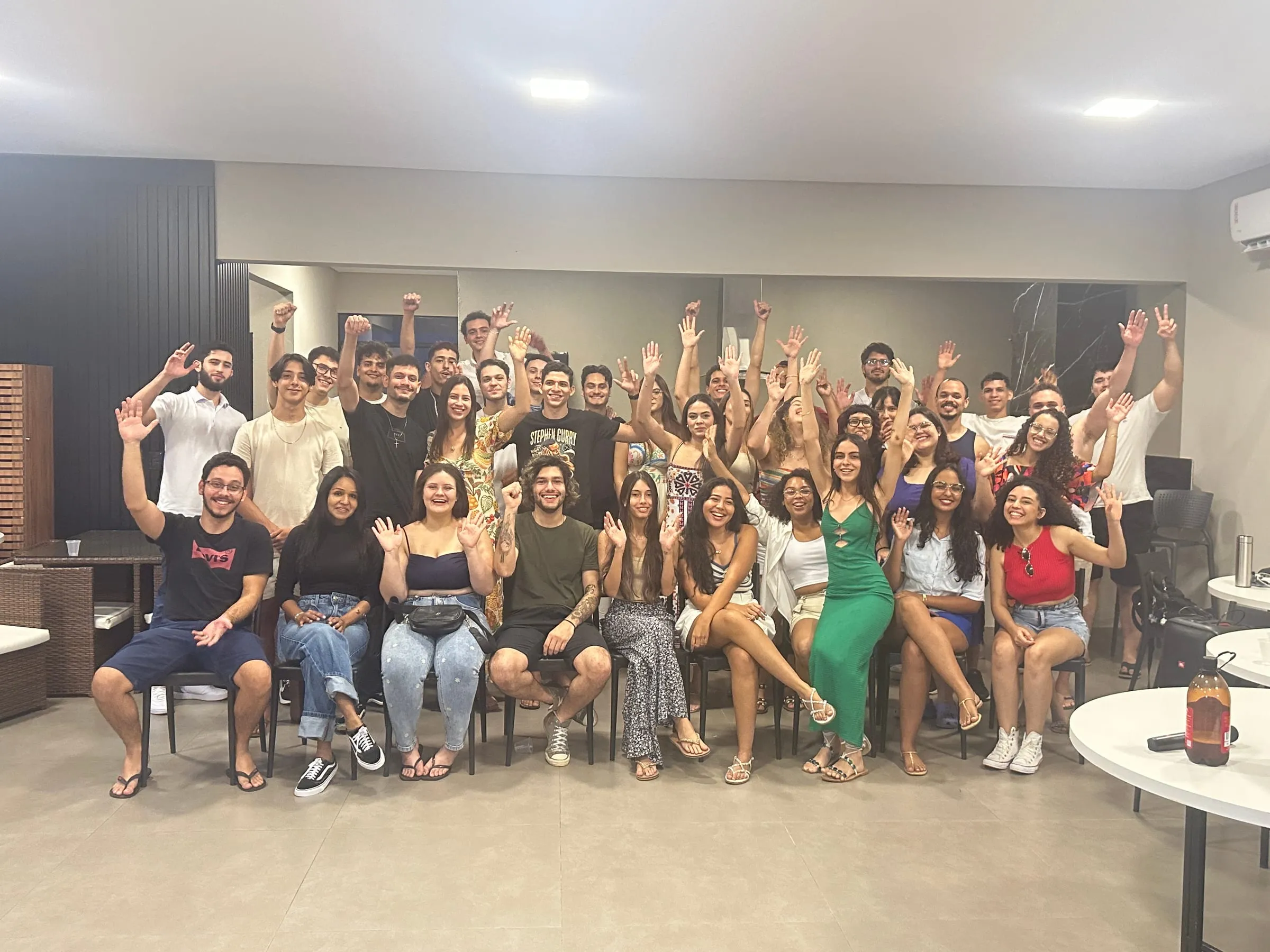 Grupo acenando para a câmera em um salão, no 4º encontro presencial
