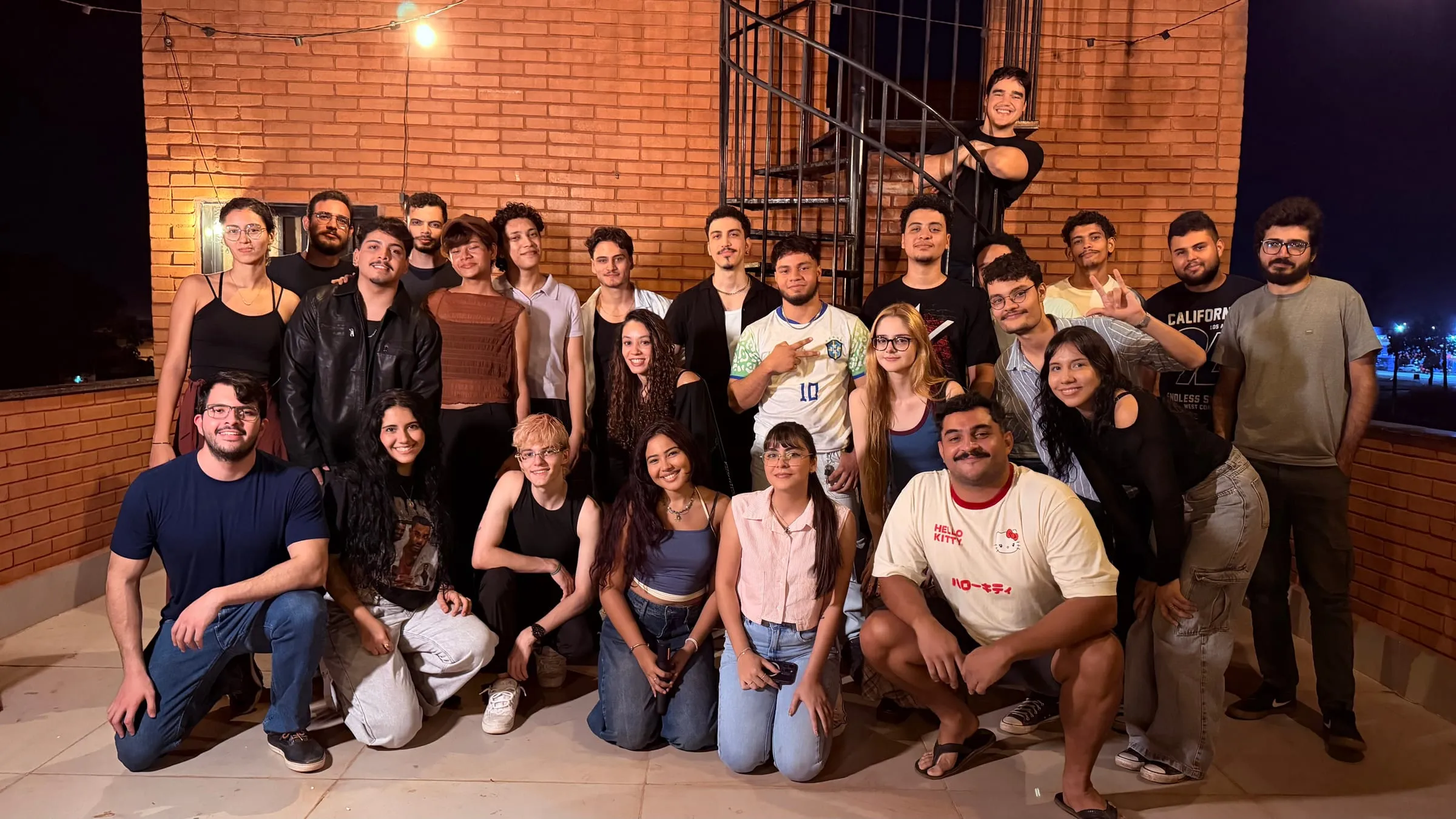 Foto em grupo à noite, diante de uma parede de tijolos, no 16º encontro presencial